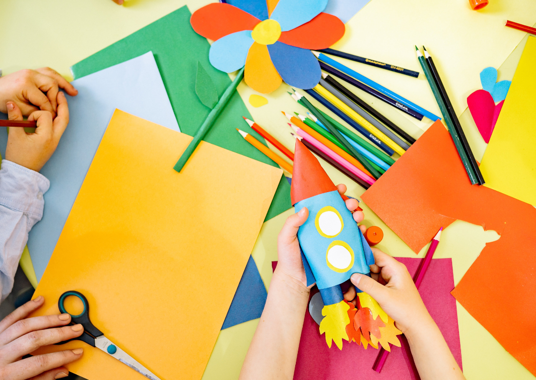Child sized hands using construction paper to craft a rocket ship and a flower.