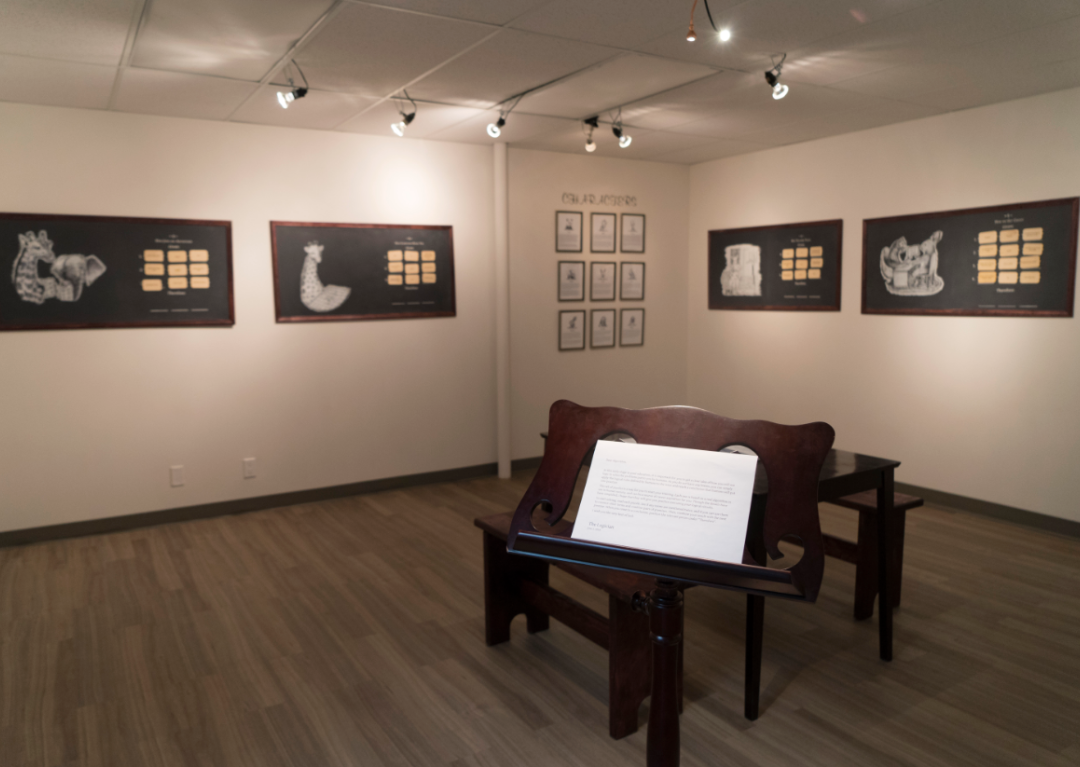 An art gallery style room where algorithmic decision artwork hangs on the walls and a wooden table sits in the centre.